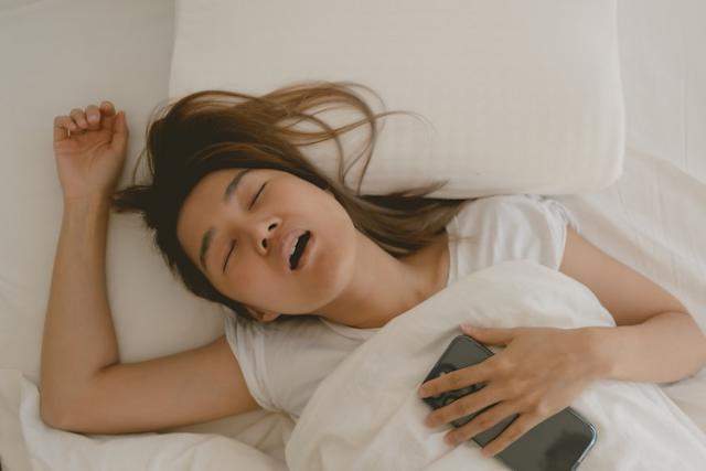 在昏暗臥室中，個人手持行動裝置、面露疲憊卻無法放下手機，真實反映現代人的「報復性熬夜」心理狀態。